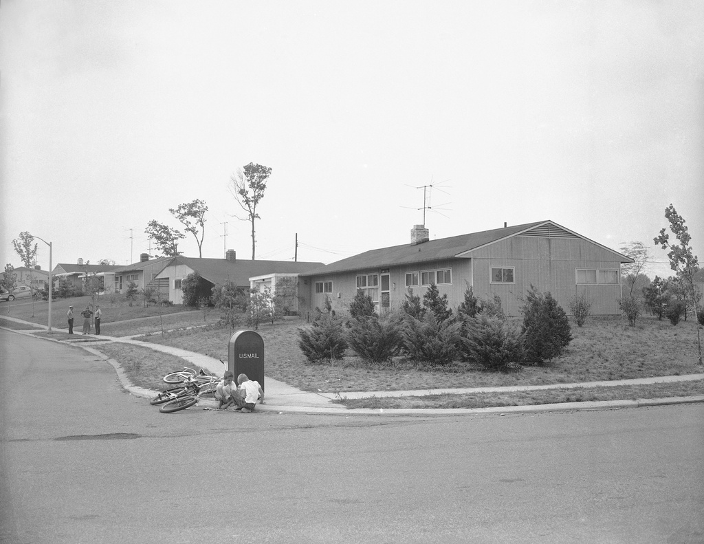 FILE - Two police patrol on the sidewalk, far left, in front of the newly-purchased home of William Myers, a black man who bought the house in this all-white community in Levittown, Penn, Aug. 16, 1957. (AP Photo/Bill Ingraham, File)