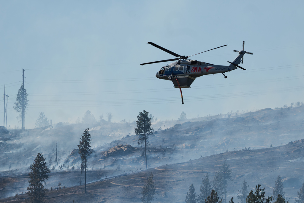 A helicopter is piloted over a burned forest after the Upriver Fire swept through on Tuesday, June 16, 2026 in Spokane, Wash. (Skyler Geissler via AP)