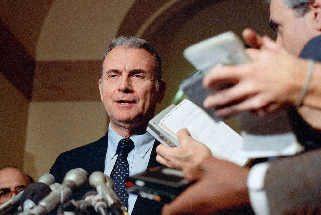 FILE - Reporters hold up tape recorders as Rep. Lee Hamilton, D-Ind., makes comments on Capitol Hill, in Washington, Dec. 18, 1986. (AP Photo/Dennis Cook, File)