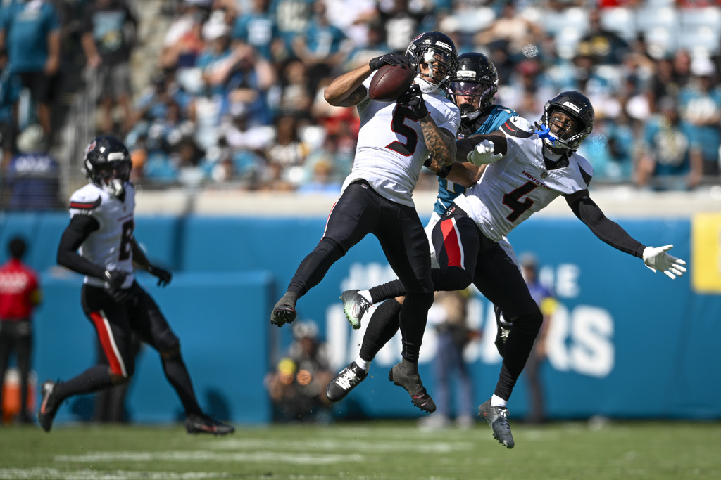 Houston Texans safety Jalen Pitre (5) intercepts a pass intended for Jacksonville Jaguars wide receiver Parker Washington, center, as teammate cornerback Kamari Lassiter (4) helps defend during the second half of an NFL football game Sunday, Sept. 21, 2025, in Jacksonville, Fla. (AP Photo/Phelan M. Ebenhack)