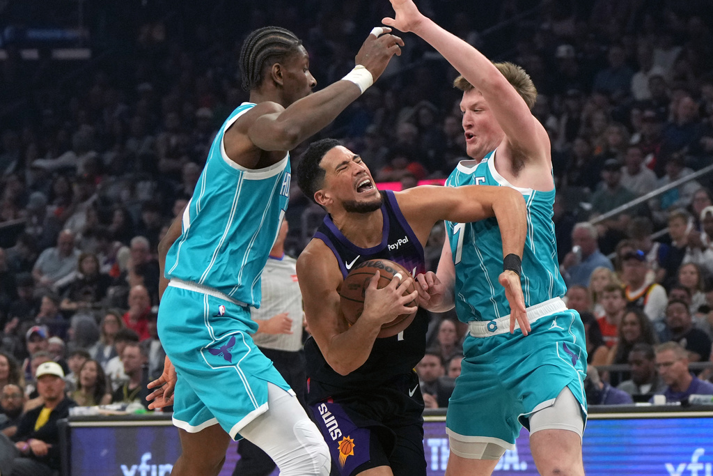 Phoenix Suns guard Devin Booker drives between Charlotte Hornets forward Moussa Diabate and guard Kon Knueppel (7) during the first half of an NBA basketball game, Sunday, March 8, 2026, in Phoenix. (AP Photo/Rick Scuteri)