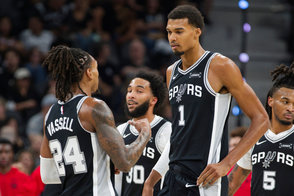 San Antonio Spurs center Victor Wembanyama (1) speaks with Spurs guard Devin Vassell (24) during the first half of their NBA basketball game against the Toronto Raptors, Monday, Oct. 27, 2025, in San Antonio. (AP Photo/Darren Abate)