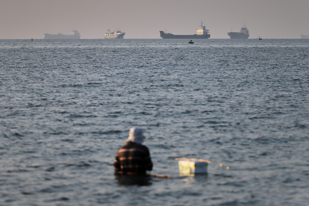 A person sits on shallow water as cargo and commercial vessels are anchored in the Strait of Hormuz off Bandar Abbas, Iran, Monday, June 8, 2026. (Amirhosein Khorgooi/ISNA via AP)