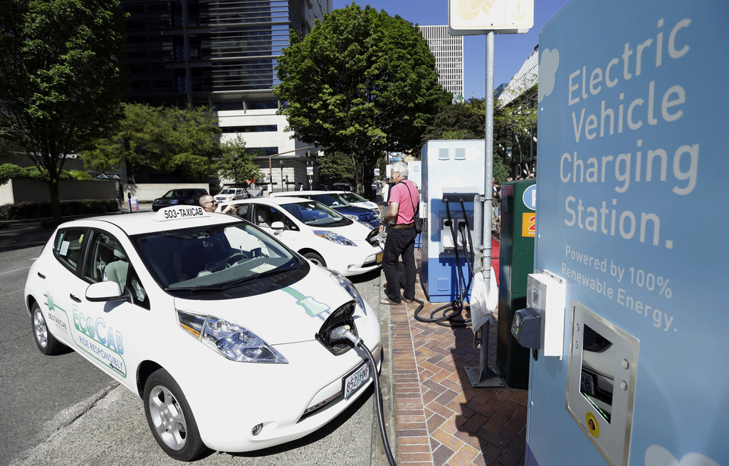FILE - A line of electric cars and newly installed charging stations sit in front of the Portland General Electric headquarters building on July 28, 2015, in Portland, Ore. (AP Photo/Don Ryan, File)