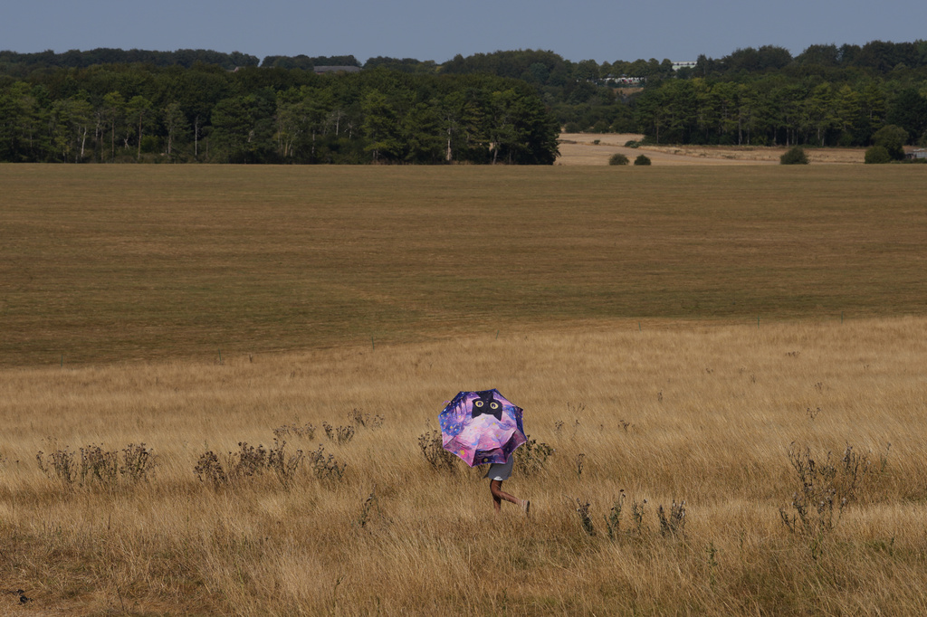 A person holds an umbrella and walks through dry grass at Stonehenge in Wiltshire, England, Thursday, Aug. 13, 2026. (AP Photo/Kin Cheung)