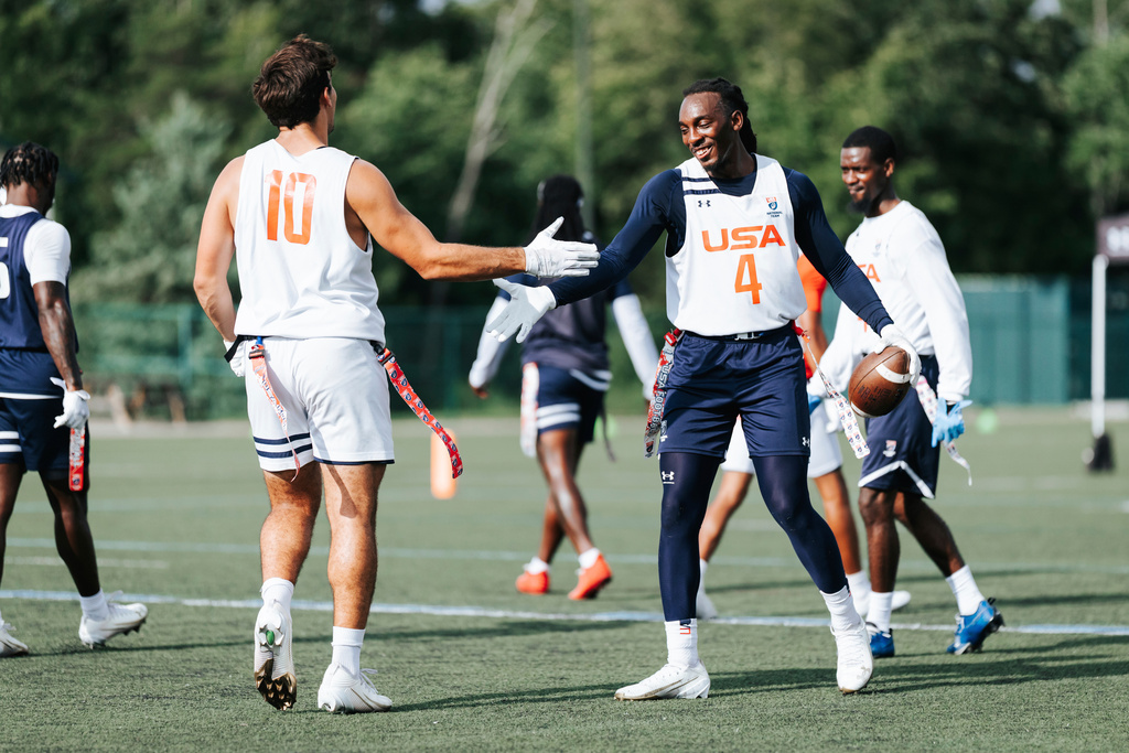 In this image provided by USA Football, Laval Davis, right, slaps hands with a teammate during flag football practice for the United States national team in Charlotte, N.C. (Lester Barnes/USA Football via AP)