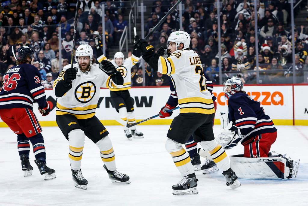 Boston Bruins' Elias Lindholm (28) and Pavel Zacha (18) celebrate David Pastrnak's goal against Winnipeg Jets goaltender Eric Comrie (1) during the first period of an NHL hockey game in Winnipeg, Manitoba, Thursday, Dec. 11, 2025. (John Woods/The Canadian Press via AP)