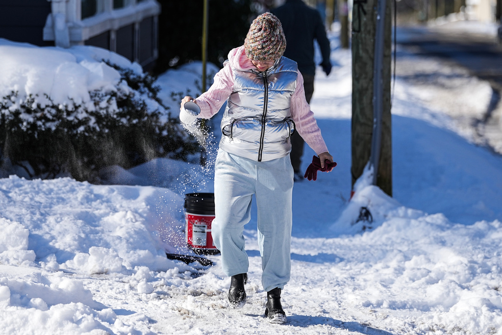 A woman spreads salt alongside the sidewalk, Sunday, Feb 1, 2026, in Charlotte, N.C. (AP Photo/Matt Kelley)