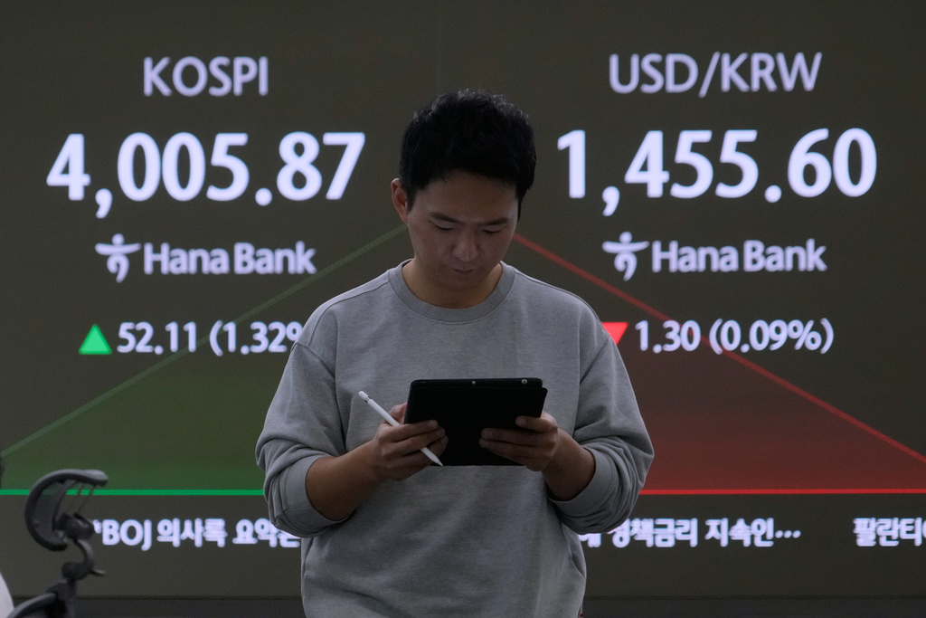 A currency trader passes by a screen showing the Korea Composite Stock Price Index (KOSPI), left, and the foreign exchange rate between U.S. dollar and South Korean won at the foreign exchange dealing room of the Hana Bank headquarters in Seoul, South Korea, Monday, Nov. 10, 2025. (AP Photo/Ahn Young-joon)