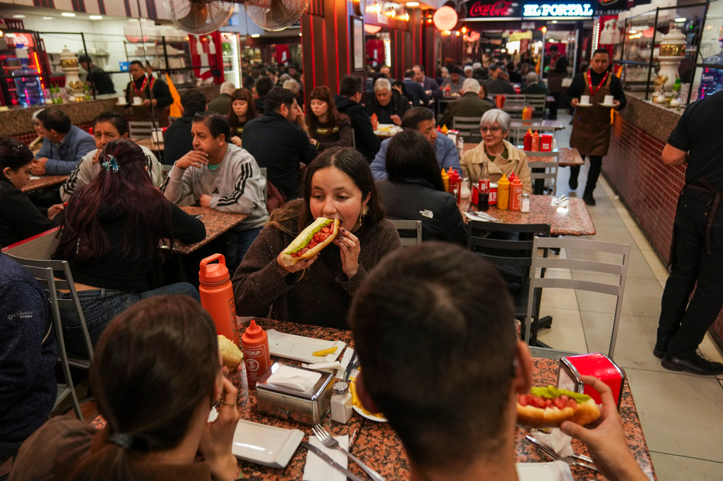 Antonia Bravo eats a "completos", traditional Chilean hot dogs topped with mashed avocado, diced tomatoes and mayonnaise, at the "El Portal Ex Bahamondes" restaurant in downtown Santiago, Chile, Thursday, Sept. 10, 2026. (AP Photo/Esteban Felix)