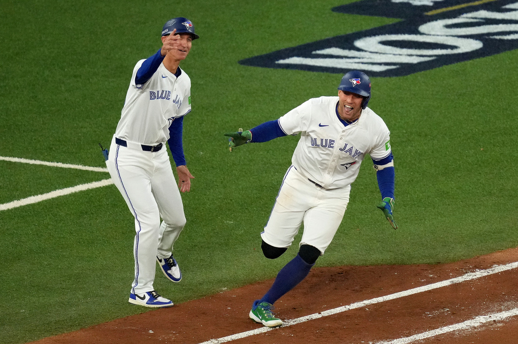 Toronto Blue Jays first base coach Mark Budzinski, left, cheers on George Springer, right, who rounds the bases after hitting a three-run home run against the Seattle Mariners during the seventh inning in Game 7 of baseball's American League Championship Series in Toronto, Monday, Oct. 20, 2025. (Chris Young/The Canadian Press via AP)