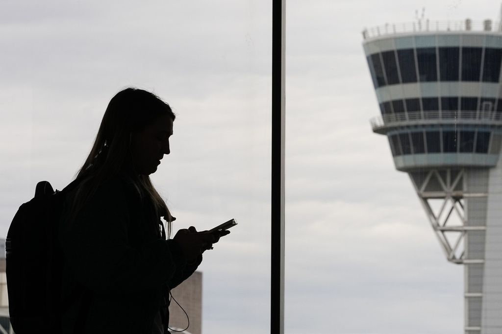 FILE - A traveler with a smartphone walks past an air traffic control tower at Philadelphia International Airport in Philadelphia on March 27, 2026. (AP Photo/Matt Rourke, File)