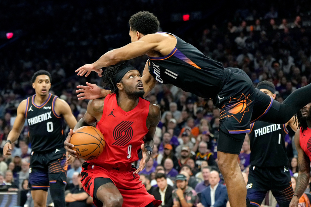 Portland Trail Blazers forward Jerami Grant (9) gets fouled by Phoenix Suns forward Oso Ighodaro (11) as Suns forward Ryan Dunn (0) looks on during the first half of an NBA play-in tournament basketball game, Tuesday, April 14, 2026, in Phoenix. (AP Photo/Ross D. Franklin)