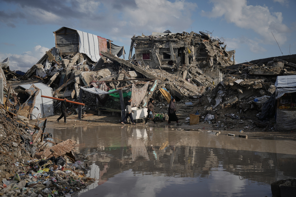 Palestinians walk among the ruins of destroyed buildings north of Gaza City Tuesday, Nov. 25, 2025. (AP Photo/Jehad Alshrafi)