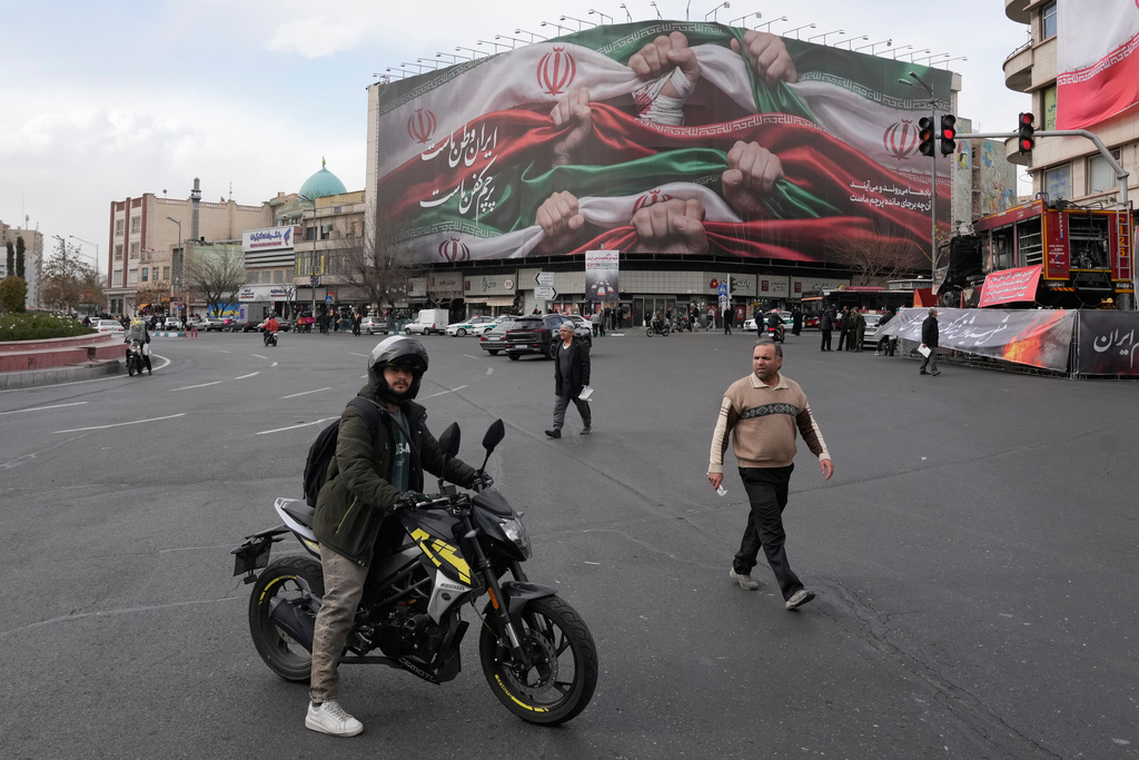 A man stands with his motorbike in front of a huge banner showing hands holding Iranian flags as a sign of patriotism, in Tehran, Iran, Wednesday, Jan. 14, 2026. (AP Photo/Vahid Salemi)
