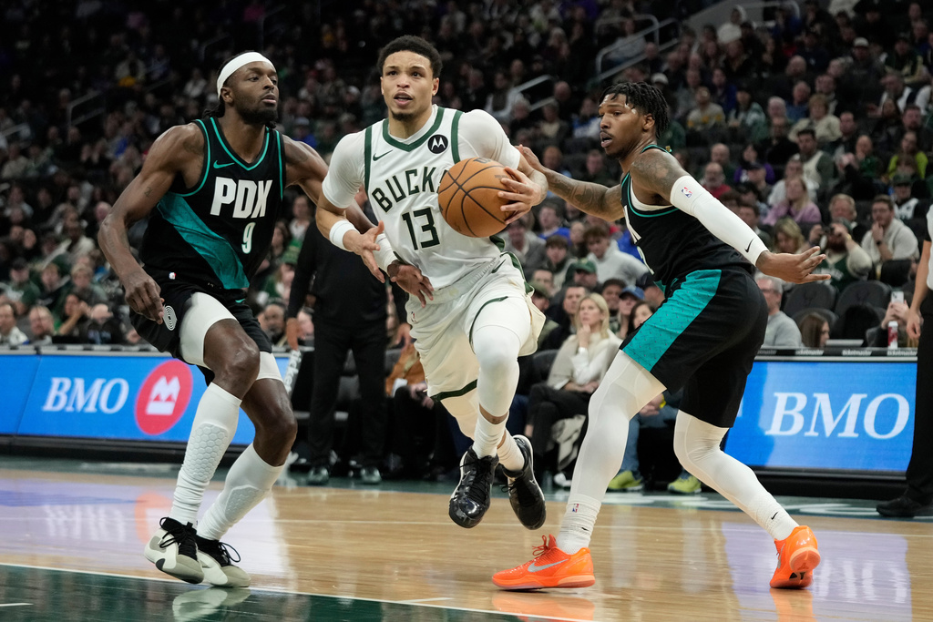 Milwaukee Bucks' Ryan Rollins (13) drives to the basket between Portland Trail Blazers' Jerami Grant (9) and Caleb Love (2) during the first half of an NBA basketball game Monday, Nov. 24, 2025, in Milwaukee. (AP Photo/Aaron Gash)