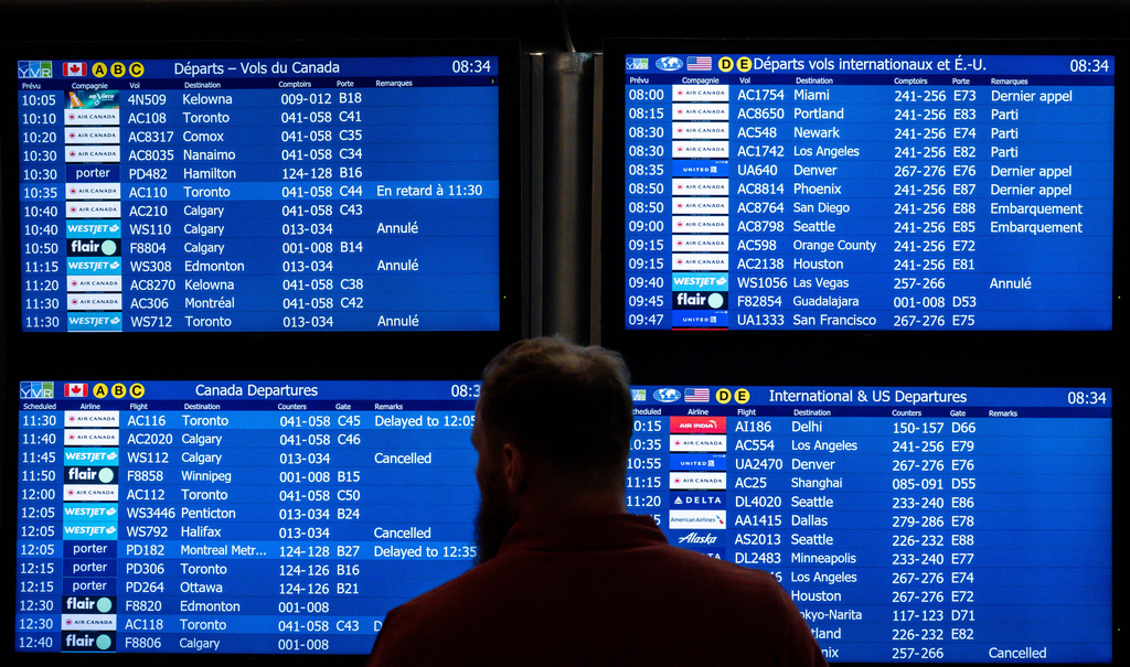 A traveller looks to an information board as WestJet flights are cancelled at Vancouver International Airport in Richmond, British Columbia, Sunday, Aug. 2, 2026. (Ethan Cairns/The Canadian Press via AP)