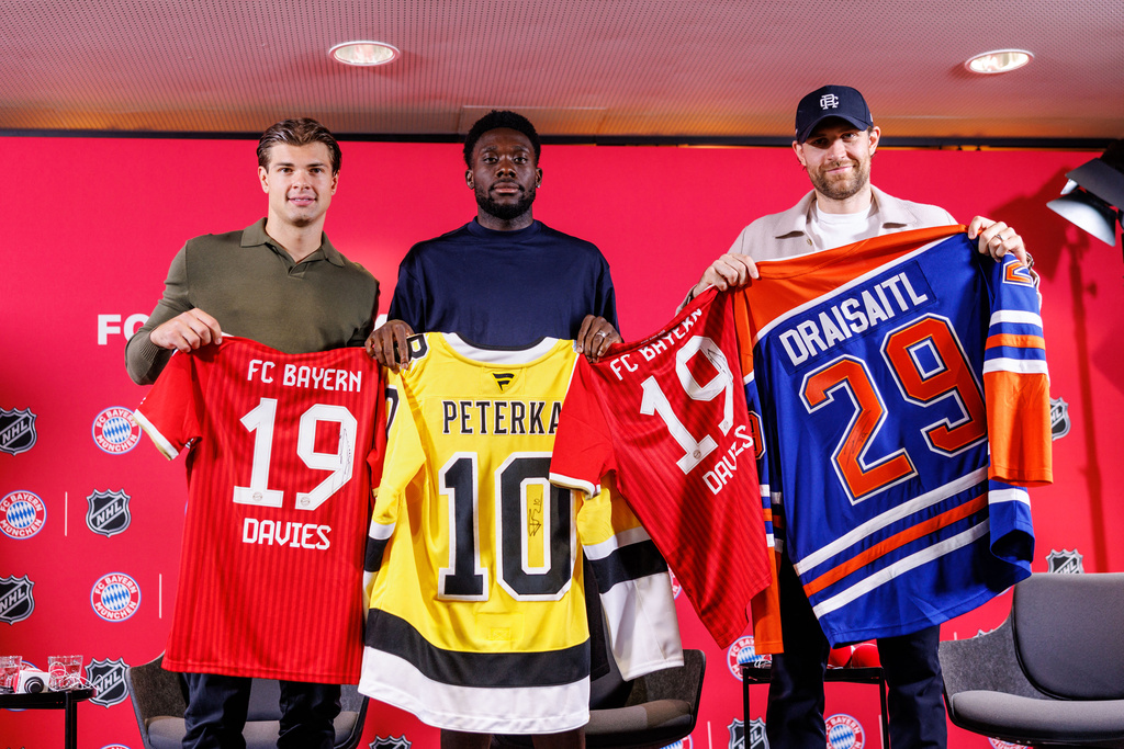 Boston Bruins’ John-Jason Peterka, from left, FC Bayern Munich’s Alphonso Davies, and Edmonton Oilers Leon Draisaitl, pose with jerseys during a joint press conference by FC Bayern Munich and the National Hockey League, Thursday, Aug. 20, 2026, in Munich. (Matthias Balk/dpa via AP)