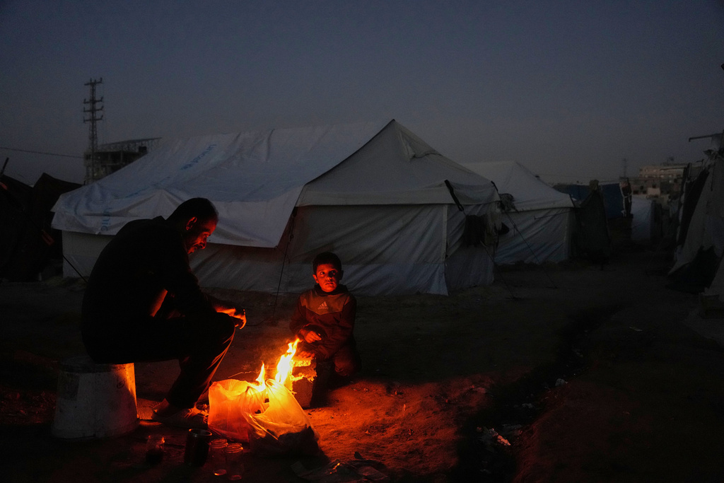 Displaced Palestinian Salah al-Mabhouh, 40, sits by the fire with his son Abdul-Razzaq 8, next to their tent in al-Bureij camp, central Gaza Strip, Wednesday, Dec. 24, 2025. (AP Photo/Abdel Kareem Hana)