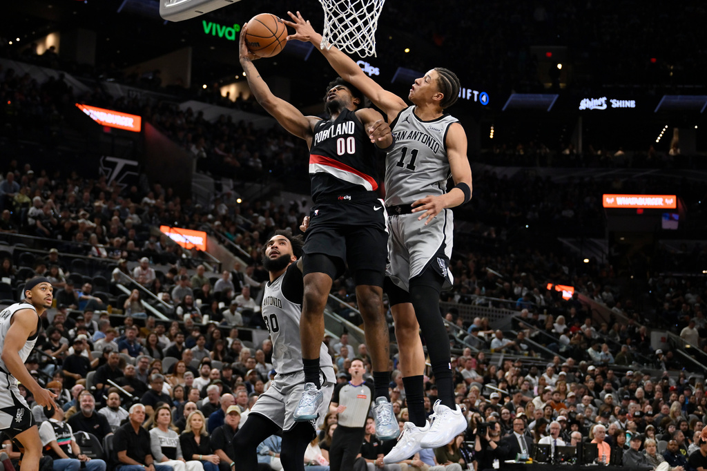 Portland Trail Blazers guard Scoot Henderson (00) is fouled by San Antonio Spurs forward Carter Bryant during the first half of an NBA basketball game, Wednesday, April 8, 2026, in San Antonio. (AP Photo/Darren Abate)