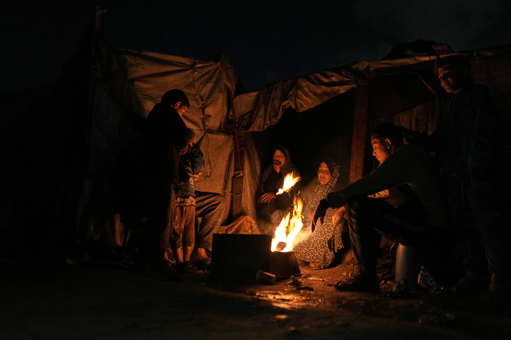 Displaced Palestinians warm themselves around a fire at a tent camp in Gaza City, Sunday, Jan. 18, 2026. (AP Photo/Jehad Alshrafi)