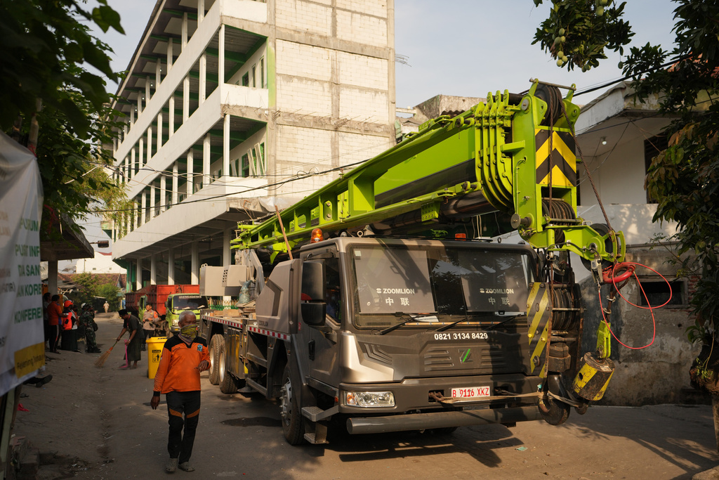 A rescuer walks past a crane prepared for the search of missing people of a building that collapsed at an Islamic boarding school in Sidoarjo, East Java, Indonesia, Saturday, Oct. 4, 2025. (AP Photo/Achmad Ibrahim)