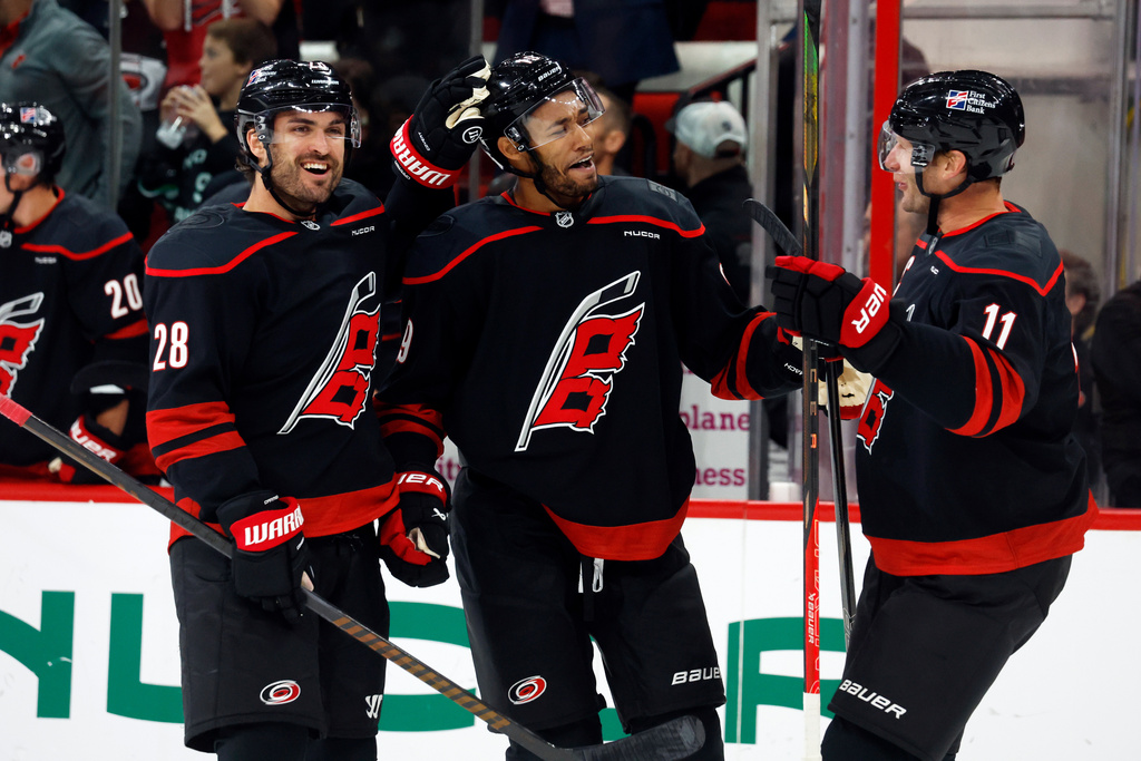 Carolina Hurricanes' K'Andre Miller, center, celebrates with teammates William Carrier (28) and Jordan Staal (11) after his goal during the second period of an NHL hockey game against the New Jersey Devils in Raleigh, N.C., Thursday, Oct. 9, 2025. (AP Photo/Karl DeBlaker)