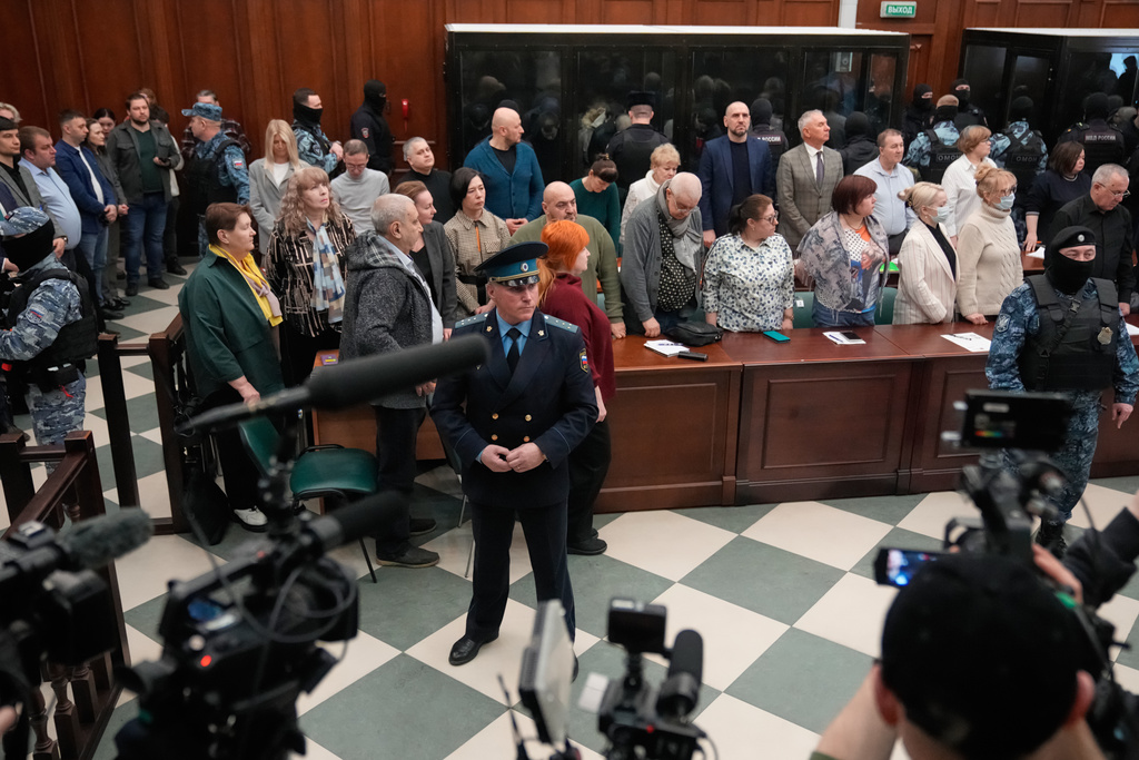 Men tried on the charges of involvement in a terror attack at the Crocus City Hall in March 2024, background, listen to the verdict from behind a glass cage as lawyers and journalists stand around at the Second Western District Military Court in Moscow, Russia, Thursday, March 12, 2026. (AP Photo/Pavel Bednyakov)
