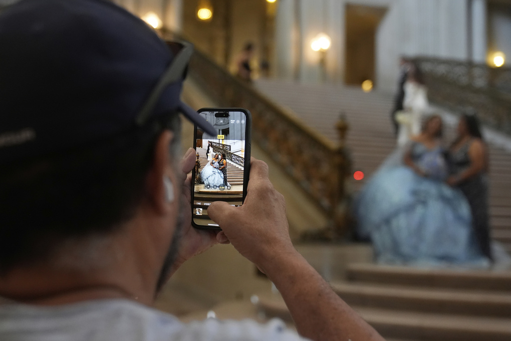 William Umanzor takes a cell phone image of his girlfriend Anna Gonzalez and her daughter Abbie Gonzalez as Abbie gets her quinceañera portrait session done at City Hall in San Francisco, Monday, Aug. 25, 2025. (AP Photo/Jeff Chiu)