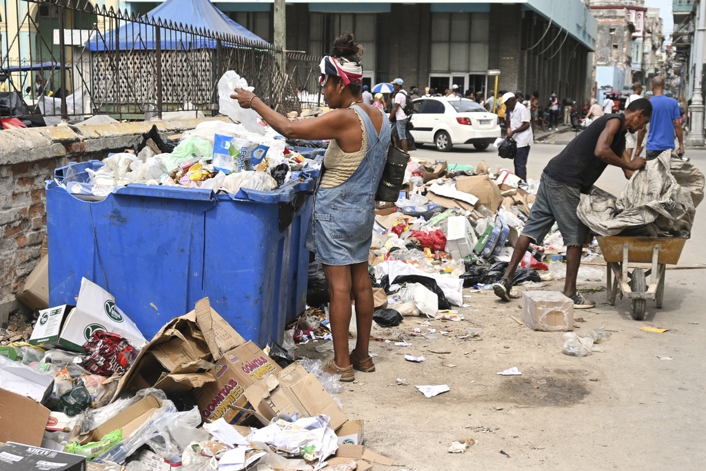 A woman searches through a dumpster looking for useful items, in Havana, Cuba, Tuesday, July 15, 2025. (AP Photo/Jorge Luis Baños)