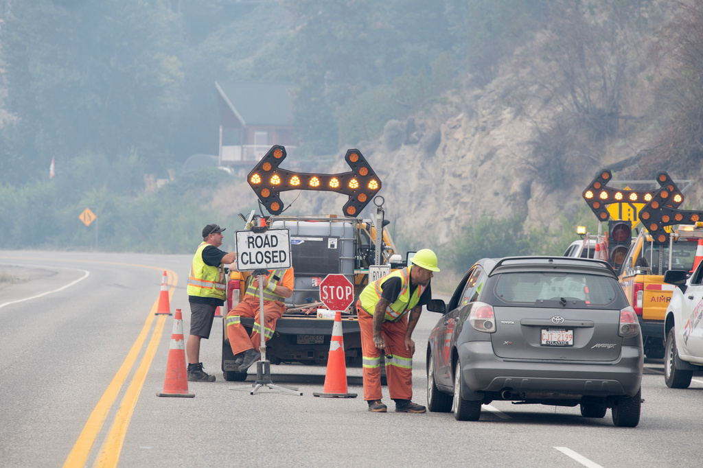 Emergency crews talk to the driver of a car at a closed section of Highway 97 south of Peachland, British Columbia, Canada, on Saturday, Aug. 8, 2026. (Gary Nylander/The Canadian Press via AP)