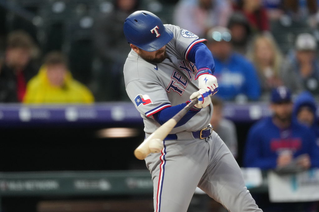 Texas Rangers' Jake Burger connects for an RBI single off Colorado Rockies relief pitcher Tanner Gordon in the second inning of a baseball game Tuesday, May 19, 2026, in Denver. (AP Photo/David Zalubowski)