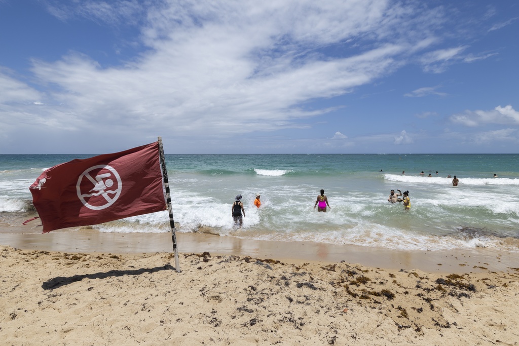 A warning flag flies on the beach as people swim in Condado, Puerto Rico, as Hurricane Erin approaches, Friday, Aug. 15, 2025. (AP Photo/Alejandro Granadillo)