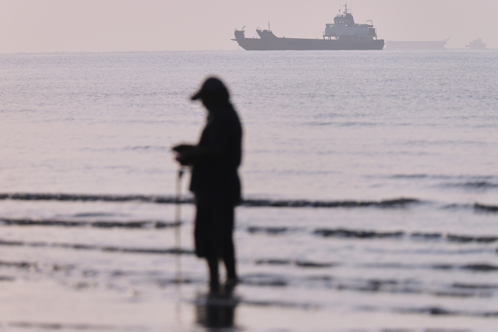 Cargo ships and service vessels are anchored in the Strait of Hormuz, as a person stands in shallow water, off Bandar Abbas, Iran, Sunday, May 31, 2026. (Amirhosein Khorgooi/ISNA via AP)