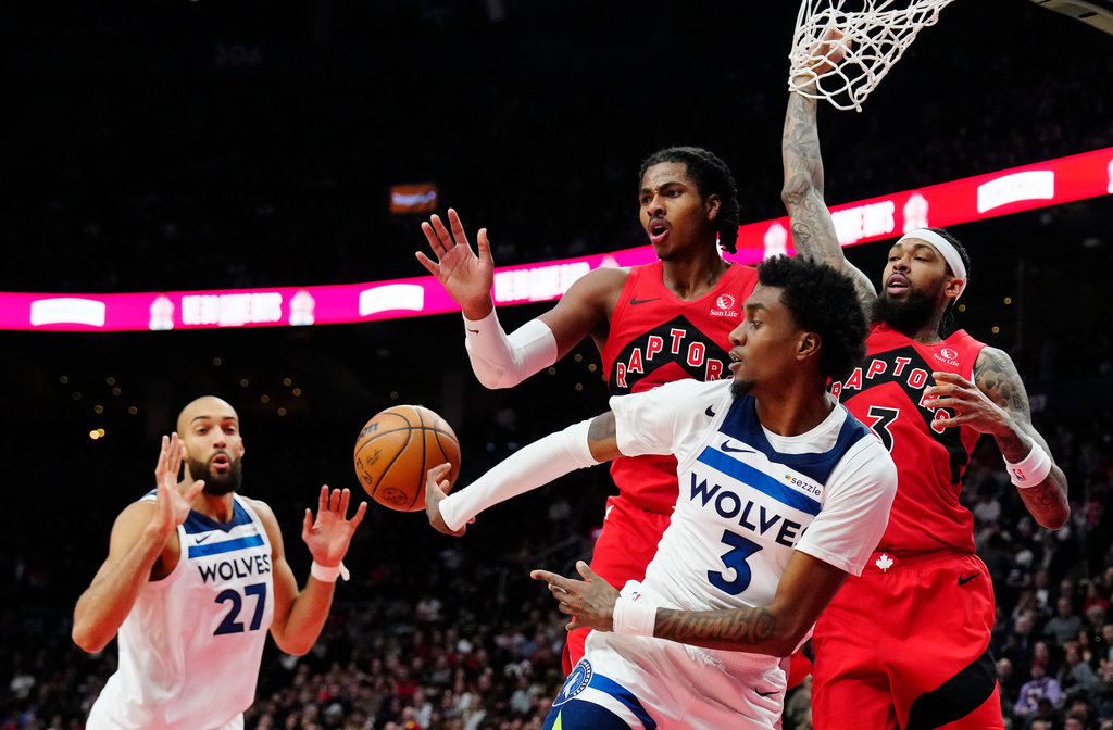 Minnesota Timberwolves' Jaden McDaniels (3) passes to Rudy Gobert (27) as Toronto Raptors' Collin Murray-Boyles (top left) and Brandon Ingram (right) defend during the first half of an NBA basketball game in Toronto, Wednesday, Feb. 4, 2026. (Frank Gunn/The Canadian Press via AP)