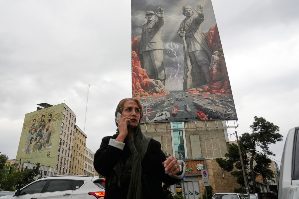 A woman talks on her cellphone as she walks past a billboard showing Rais Ali Delvari, a national hero in an early 1900 uprising against British forces in southern Iran in the Persian Gulf, right, and the late Revolutionary Guard's navy chief Alireza Tangsiri, who was killed in the U.S.-Israeli strike in late March 2026, commanding the closure of the Strait of Hormuz, on a building at a square in downtown Tehran, Iran, Monday, April 20, 2026. (AP Photo/Vahid Salemi)