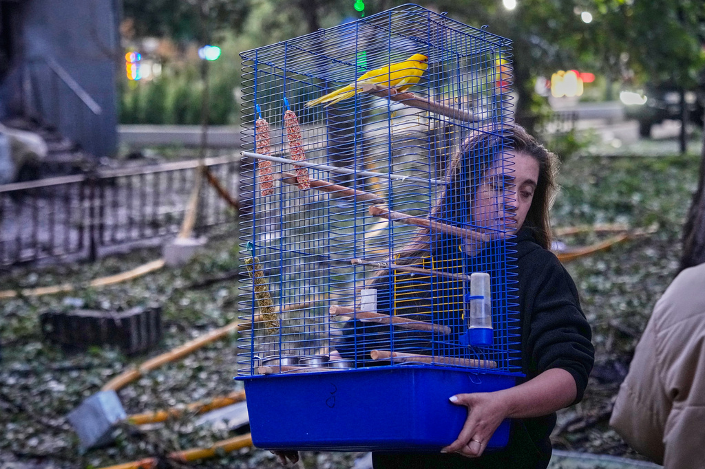 A woman carries a cage with a parrot as she leaves her damaged house following a Russia missile attack in Kyiv, Ukraine, Sunday, July 19, 2026. (AP Photo/Efrem Lukatsky)