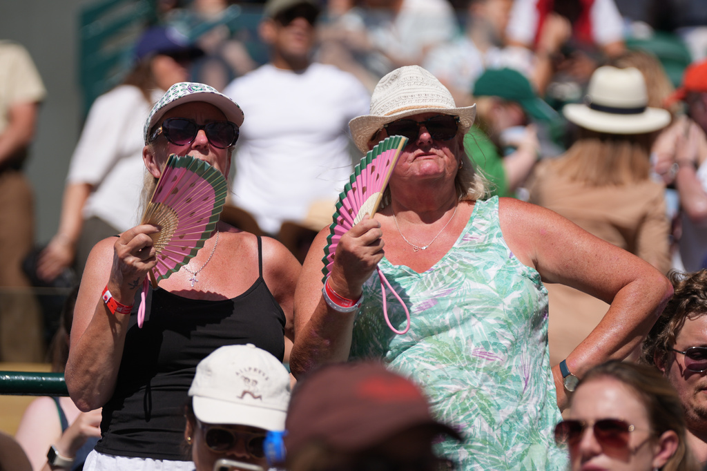 Spectators cool themselves with a hand fan as they watch the second round men's singles match between Alexander Zverev of Germany and Valentin Royer of France, at the Wimbledon Tennis Championships in London, Thursday, July 2, 2026. (AP Photo/Maja Smiejkowska)