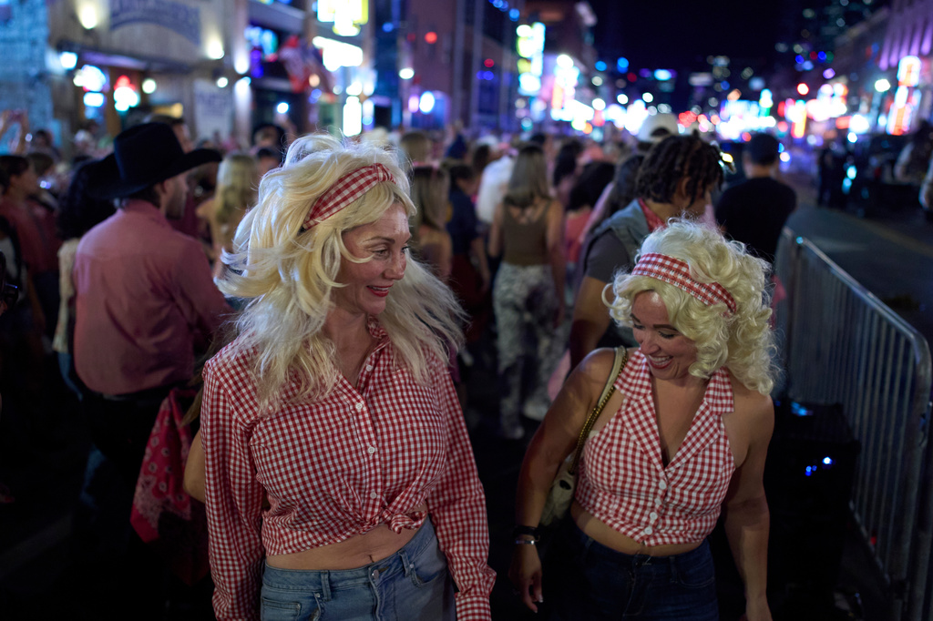 Danielle Maples, left, and Heather Lucas, right, dressed in Dolly Parton costumes dance with a flash mob on Broadway Friday, Sept. 25, 2026, in Nashville, Tenn. during a Dolly Parton Day event honoring the late country music artist. (AP Photo/George Walker IV)