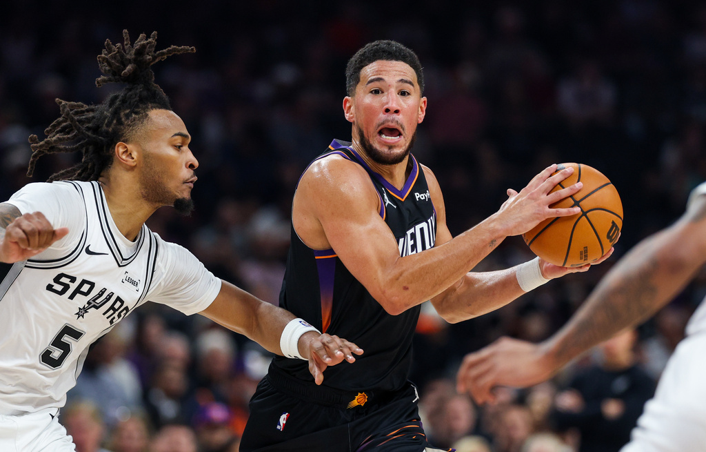 Phoenix Suns guard Devin Booker, right, looks to pass the ball as San Antonio Spurs guard Stephon Castle (5) defends during the first half of an NBA basketball game, Sunday, Nov 2, 2025, in Phoenix. (AP Photo/Mike Christy)