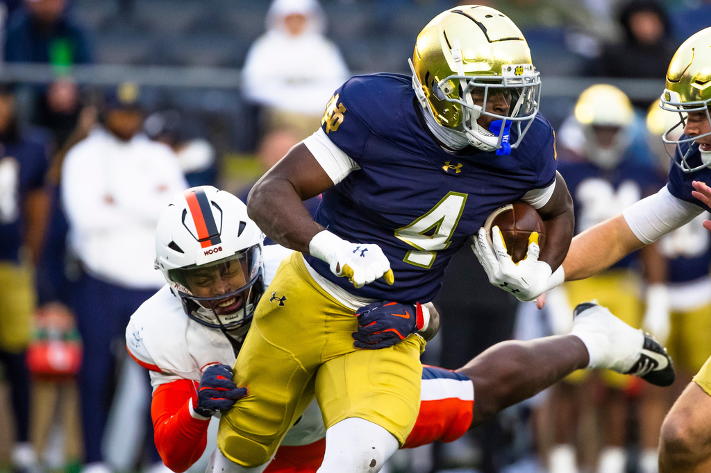 FILE - Notre Dame running back Jeremiyah Love (4) gets past a tackle-attempt by Virginia linebacker Kam Robinson, left, during the first half of an NCAA college football game Saturday, Nov. 16, 2024, in South Bend, Ind. (AP Photo/Michael Caterina, File)