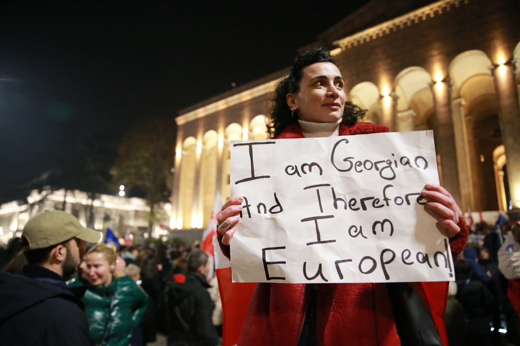 A demonstrator holds a poster during a rally in the Georgian capital of Tbilisi, on Friday, Nov. 28, 2025, to mark 365 days of non-stop protests against the government's decision to halt talks on joining the European Union. (AP Photo/Zurab Tsertsvadze)
