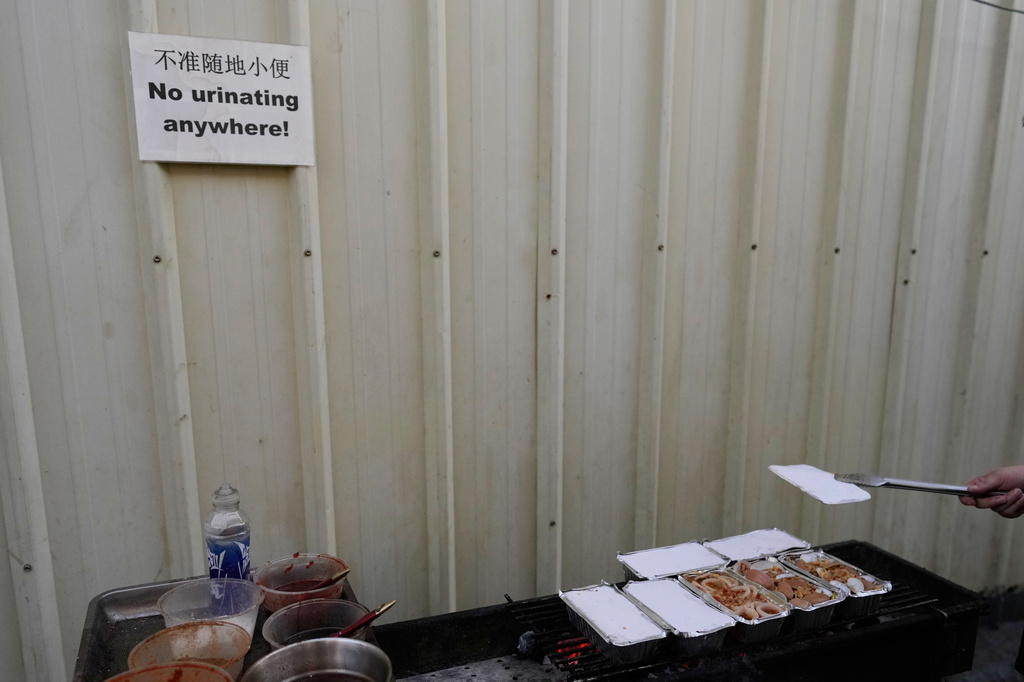 A sign warning against urinating in public is posted at the Presidential Anti-Organized Crime Commission temporary detention center, a former scam compound, as a rescued Chinese scam worker cooks outside the canteen in Pasay, Philippines, Tuesday, June 3, 2025. (AP Photo/Aaron Favila)