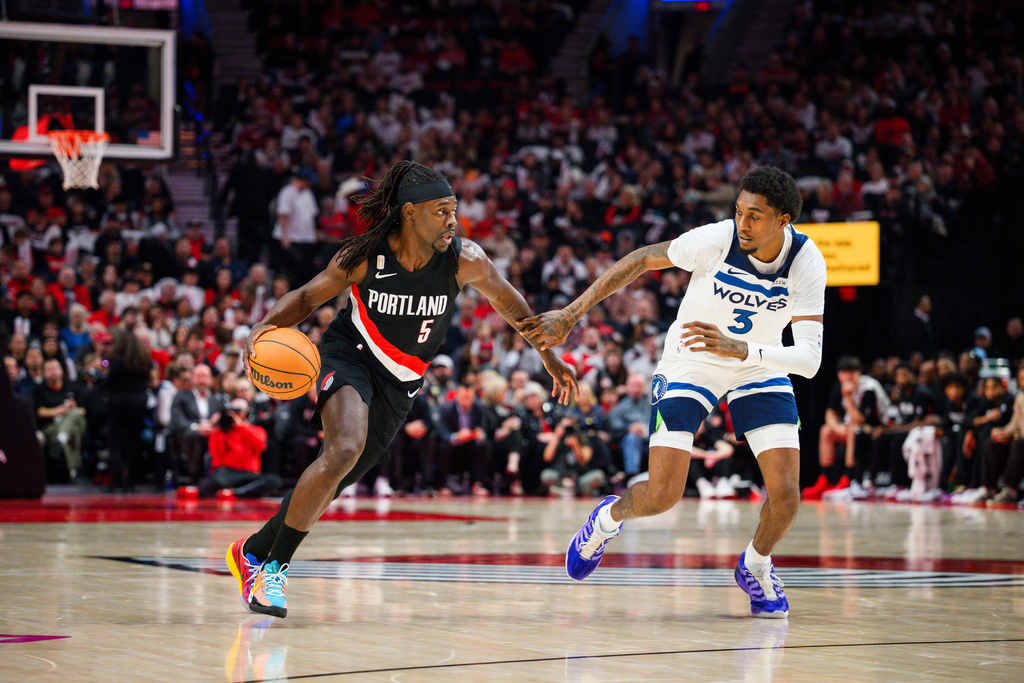 Portland Trail Blazers guard Jrue Holiday (5) drives down the court past Minnesota Timberwolves forward Jaden McDaniels (3) during the first half of an NBA basketball game on Wednesday, Oct. 22, 2025, in Portland, Ore. (AP Photo/Molly J. Smith)