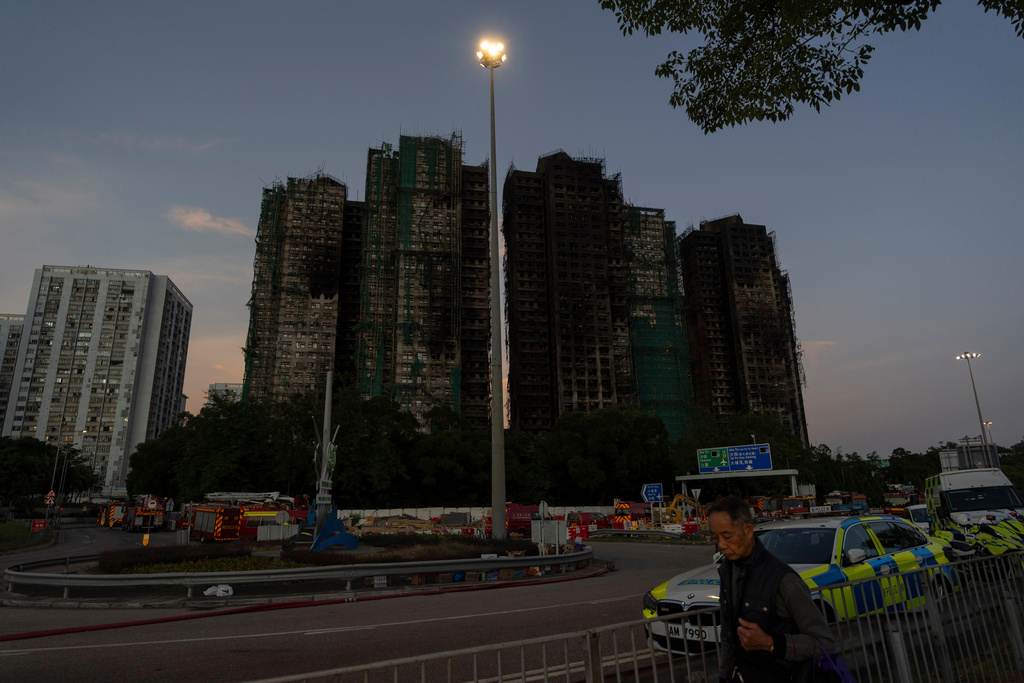 A man walks past charred buildings burnt after a deadly fire that started Wednesday at Wang Fuk Court, a residential estate in the Tai Po district of Hong Kong's New Territories, Friday, Nov. 28, 2025. (AP Photo/Ng Han Guan)