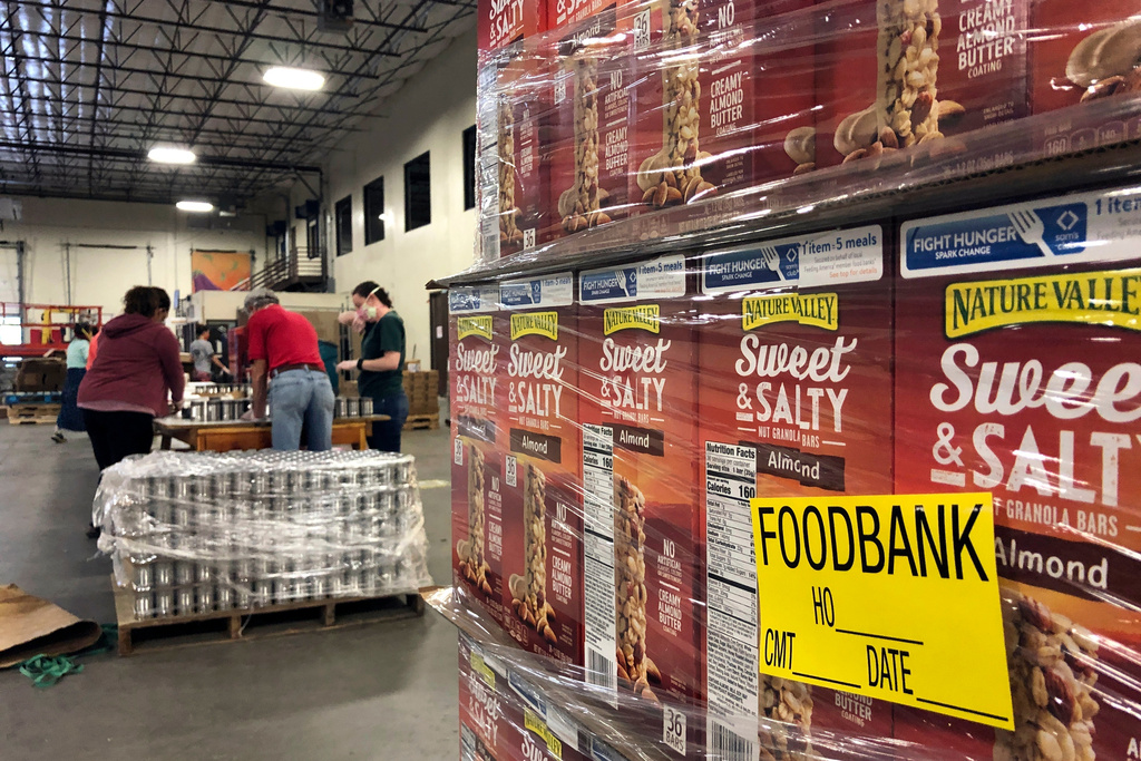 FILE - A pallet of food awaits processing as volunteers work in the background to label cans of beans for redistribution at Roadrunner Food Bank in Albuquerque, N.M., May 7, 2020. (AP Photo/Susan Montoya Bryan, File)
