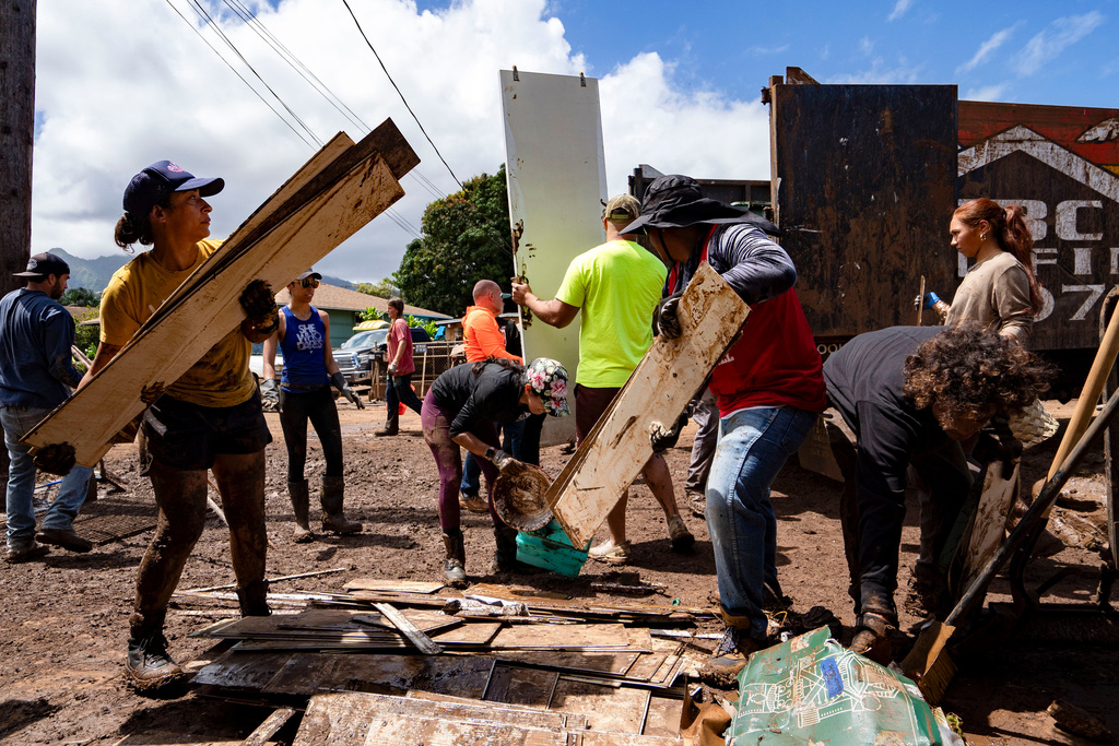 Volunteers load debris and damaged household items onto a truck during cleanup efforts following flooding, Tuesday, March 24, 2026, in Waialua, Hawaii. (AP Photo/Mengshin Lin)