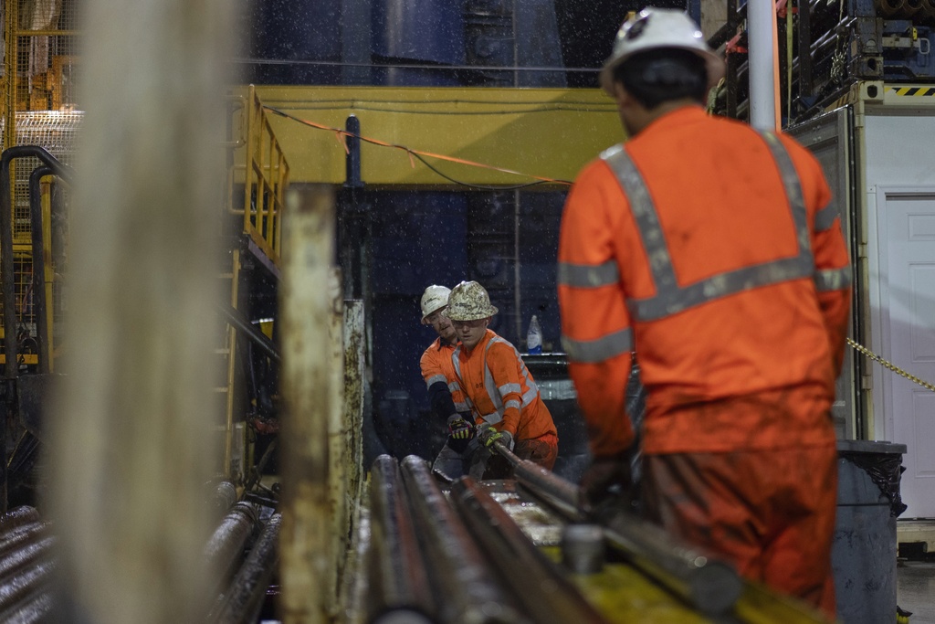 Expedition 501 drilling team members, from left, Nick Boehne, Chris Redding and Lalo Aguilar work to remove a core sample from an inner tube during a wireline core drilling operation aboard the Liftboat Robert platform, in the North Atlantic, Sunday, July 20, 2025. (AP Photo/Carolyn Kaster)