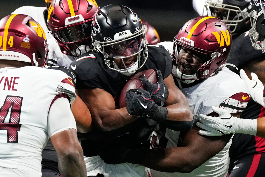 Atlanta Falcons running back Bijan Robinson, center, is tackled by Washington Commanders defenders during the first half of an NFL football game, Sunday, Sept. 28, 2025, in Atlanta. (AP Photo/Brynn Anderson)