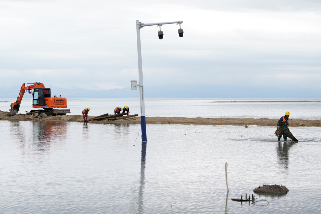 Workers clear debris around security cameras as rising waters flood a stretch of Qinghai Lake in western China's Qinghai province, Tuesday, July 1, 2025. (AP Photo/Ng Han Guan)